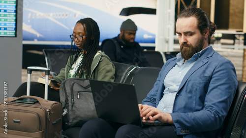 Photos Entrepreneur types on a laptop and checks a mobile phone with impatience while waiting for important notifications during an airport business trip