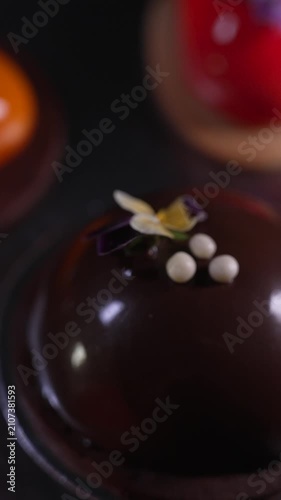 Close up of a minimalistic chocolate mousse pastry featuring a shiny mirror glaze delicately decorated with a small flower, haute cuisine, cinematic food videography
