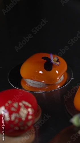 Close up of a beautifully crafted orange mousse pastry featuring a shiny mirror glaze in a professional kitchen, cinematic food videography
