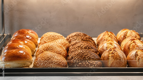 Fresh bread showcase with modern display featuring assorted rolls including sesame and multigrain varieties in bakery setting