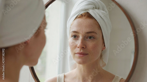 Young Woman with Towel on Head Looking in Mirror During Morning Skincare Routine and Natural Beauty Care