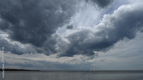 Time-lapse of storm clouds drifting across the sky above a large lake with trees along the horizon
