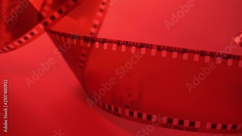 35mm negative photographic film in rotation in red room, camera darkroom. Slightly rolled film strip isolated on red background. Analog film strips. Analog photography. Close-up