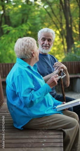 Elderly people spending time together on bench in park, camera moving