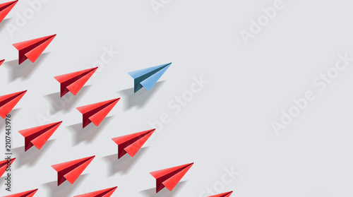 Blue paper airplane flying in a different direction from a group of red airplanes
