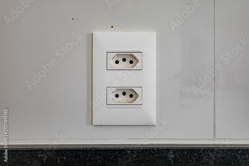 Close up of a standard double white electrical socket on a light wall in a Brazilian household