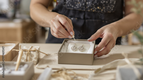Artisan packaging handmade jewelry for online orders. Traditional craftsmanship adapting to e-commerce shipping and digital sales.