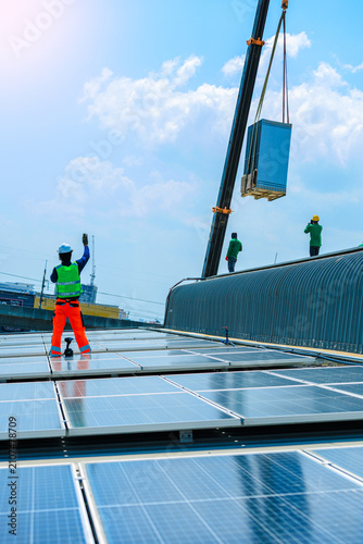 solar roof photovoltaic electricity renewable rooftop sustainable generator helmet.Crane lifts battery storage equipment onto an industrial rooftop with solar panels for a clean energy system.