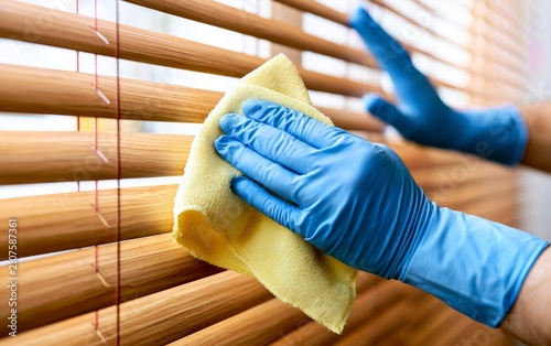 Person Cleaning Wooden Blinds in Household Environment with Yellow Cloth and Blue Gloves
