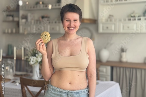 positive and surprised woman with bun in hand against kitchen background, body positive