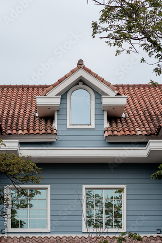 Blue house facade featuring a dormer window, terracotta tile roof, and two lower windows with white frames.