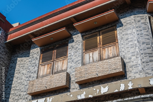 Fotografie Low angle view of traditional wooden windows on a modern grey stone tile wall facade under blue sky