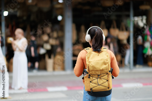 Foto Young female traveler with a yellow backpack and headphones exploring a vibrant
