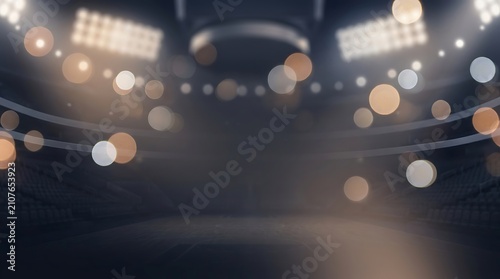 A dark stadium interior with bright, blurred lights creating a bokeh effect, suggesting an event or performance venue.