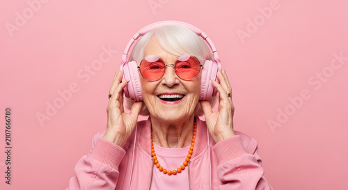 Happy senior woman wearing headphones. Elderly lady listening to music with pink glasses.