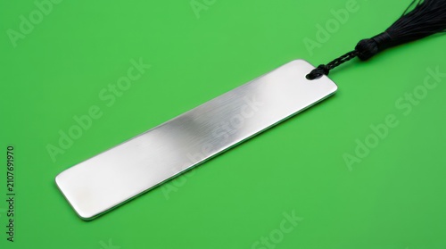 Brushed metal bookmark with black tassel on green surface