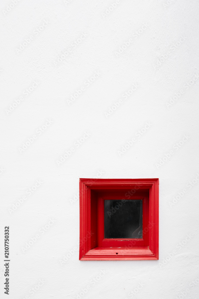 Fototapeta premium minimalist composition featuring a small, square red window frame set deep into a pristine white textured wall. The high contrast creates a bold, modern, and artistic architectural detail.
