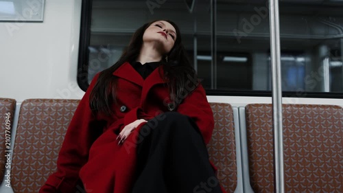 A beautiful brunette in an alizarin red coat riding the metro, urban street fashion
