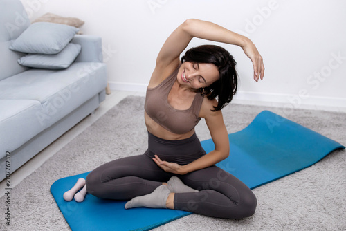 Принти на полотні Smiling mid-adult female executing cross-legged side bend fitness exercise in li