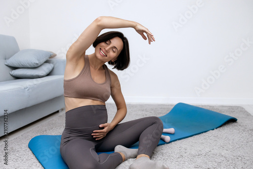 Fotografie Smiling mid-adult lady executing gentle home gymnastics for healthy gestation pe