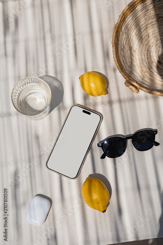 Flat Lay of Summer Essentials. Blank Smartphone Mockup Surrounded By Lemons And Sunglasses In Striped Sunlight