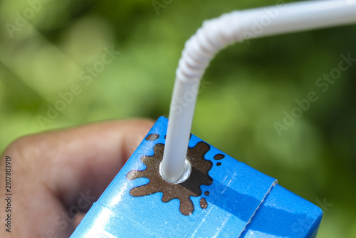 Foto Hand holding small blue drink carton with white bendy straw inserted and chocola
