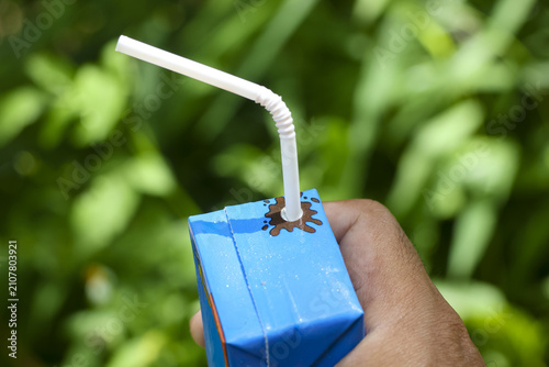 Foto Blue juice box with white bendy straw held in hand against green foliage, refres