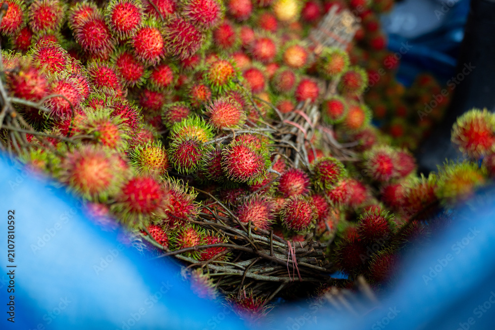 Fototapeta premium Rambutan fruit cluster red hairy tropical fruit on stems in market basket, vibrant color and fresh texture evoking summer harvest