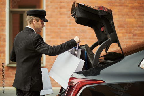 Obraz na plátně Middle aged Caucasian chauffeur loading shopping bags into car trunk, providing luxury transport and retail assistance