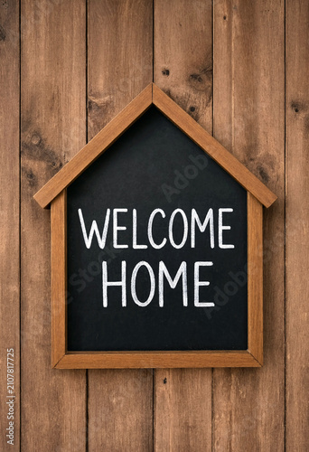 Rustic wooden welcome home sign shaped like a house on wooden wall background