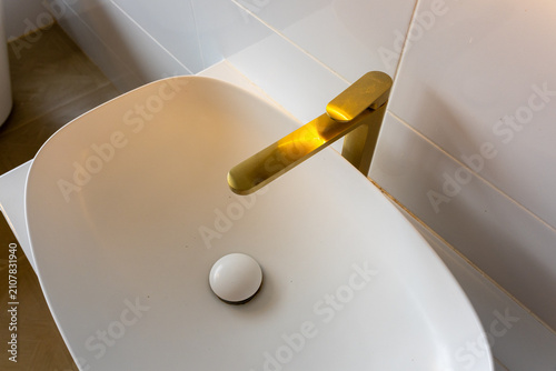 Fotografie Modern white oval bathroom sink with gold faucet and warm sunlight reflecting on