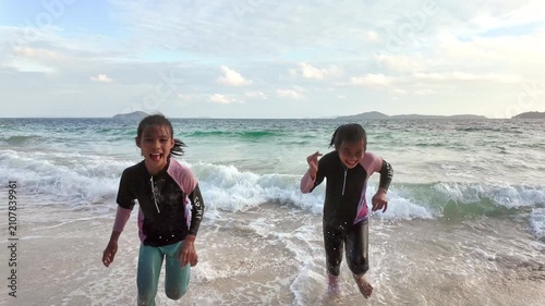 Two Asian girls playing and splashing water in ocean waves on sandy beach during summer vacation
