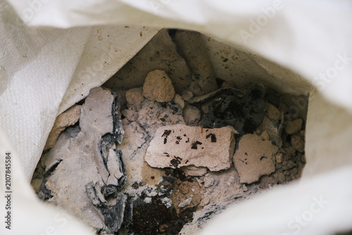 A close-up view of a bag filled with debris, including broken pieces of stone and ash. The contents appear dusty and disorganized.