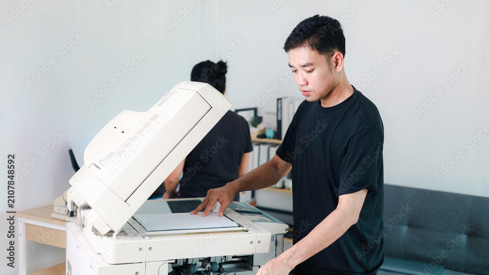 Obraz premium Young office worker operating a commercial photocopier in a modern workplace, representing document printing, copying, office technology, business services,