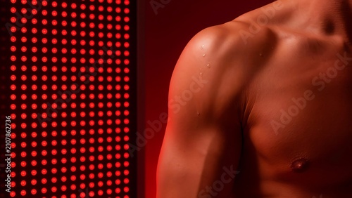 A man using red light therapy on his shoulder