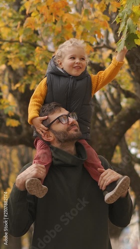 father and child playing on shoulders in autumnal outdoor setting with joyful mood and vibrant yellow leaves and brown clothing visible, side view of family bonding moment.