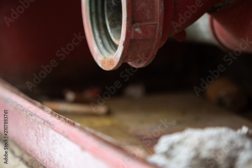Fotografía rusty metal pipe attached to red structure in deteriorating industrial environment close-up perspective