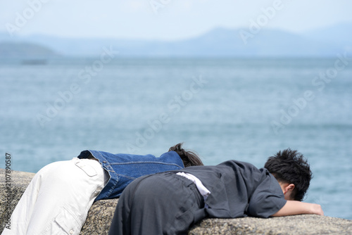 фотографія Young man rests on stone ledge by calm sea