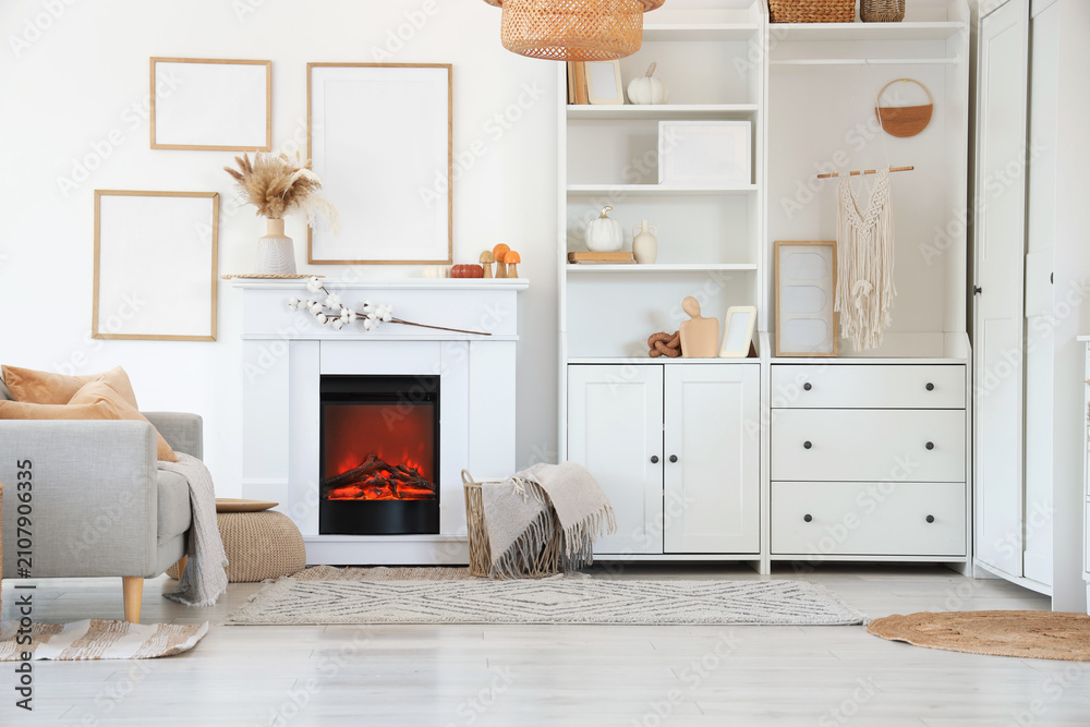 Obraz premium Interior of living room with grey sofa, coffee table, shelving units and autumn home decor on fireplace near white wall