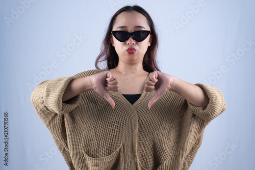 Konstfotografi Young Asian woman in sunglasses giving double thumbs down on white studio backgr