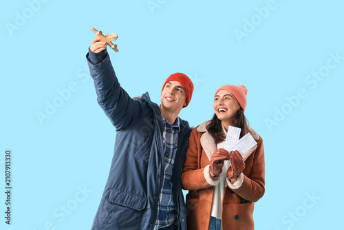 Cute young couple in warm clothes with wooden plane and tickets on blue backg...