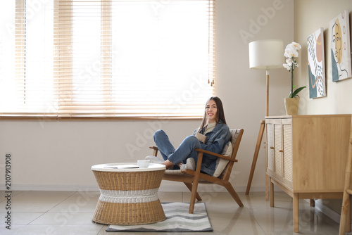 Young woman sitting in armchair with book near coffee table in room