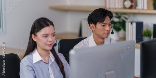 Asian male call center agent wearing headset working at office computer