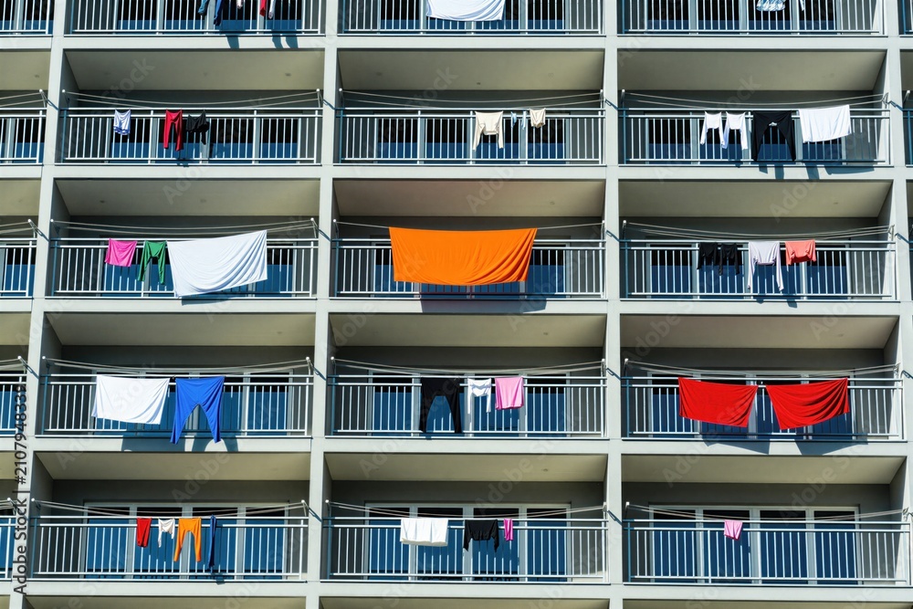 Obraz premium Clothes dry on lines strung across balconies of modern condo building. Laundry hangs on railings under bright sun, showing colorful garments, textiles on apartment terraces. Residential laundry dries