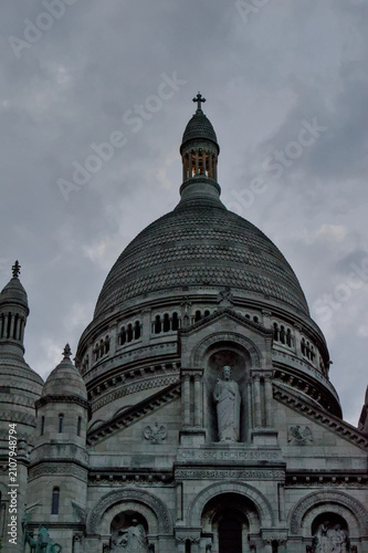 Fotografie Dramatic close-up architectural view of the Sacre Coeur Basilica domes and statue in Montmartre, Paris, under a cloudy sky