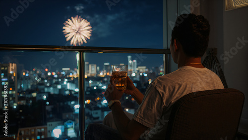 Obraz w ramie 自宅のバルコニーの椅子に座り冷たいビールグラスを手に持って遠くに上がる花火を見る男性