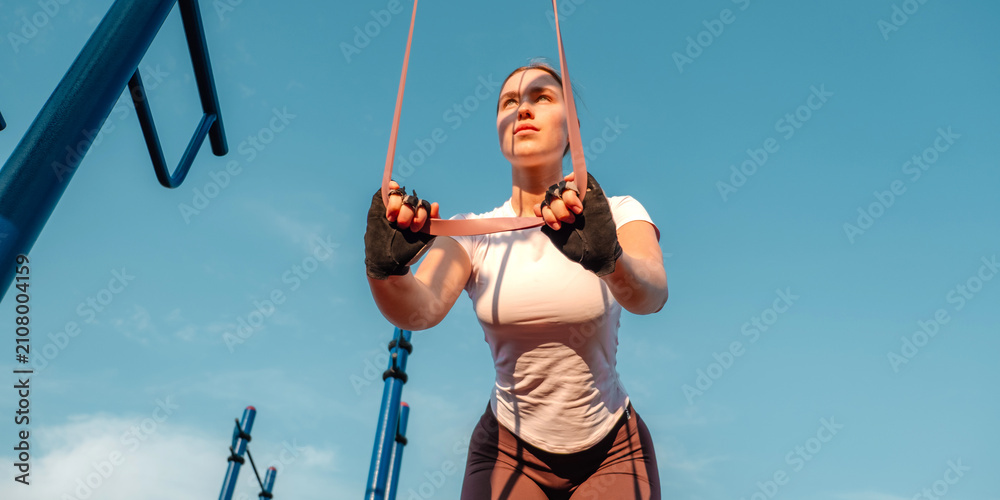 Obraz premium Woman setting up resistance band on outdoor gym bar, functional fitness and no gym workout preparation at golden hour