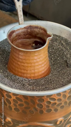 Traditional Turkish coffee being prepared on hot sand in a copper cezve.