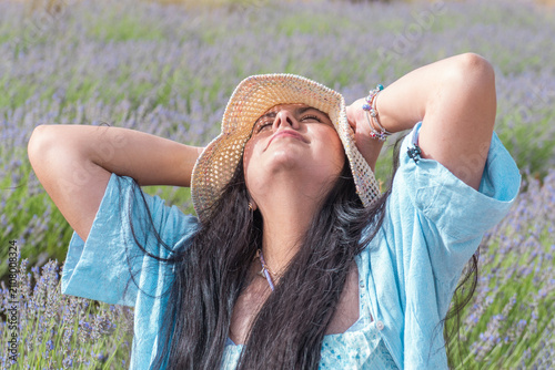 Schilderij op canvas A young woman in a straw hat enjoys the sun, its scent, freedom among blooming lavender in a field