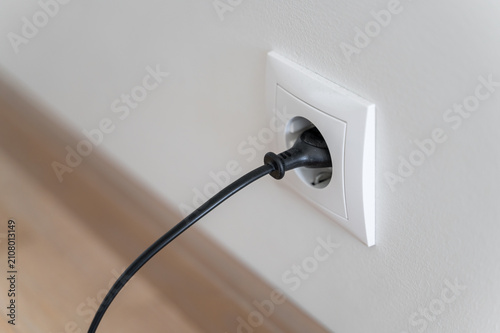 White wall socket with black plug and cable inserted, home electricity and everyday life